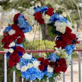 Heart-shaped floral wreath with red roses, white roses, blue hydrangeas, and white lilies