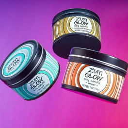 Three scented candles in black tins on a pink-purple background