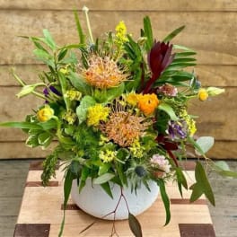 Mixed floral arrangement in a white bowl vase with yellow, burgundy, and purple blooms