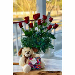 Red roses in a vase with a teddy bear and gift box