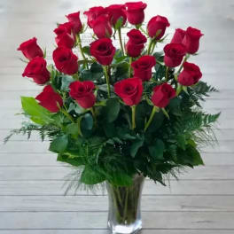 Red roses arranged in a clear glass vase with greenery