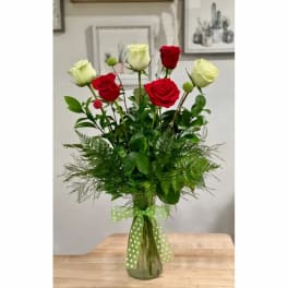 Red and white roses in a glass vase with a green polka-dot ribbon