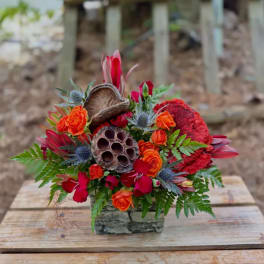 Bright orange and red floral arrangement in a stone container with natural pods