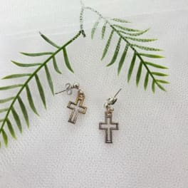 Pair of cross earrings on a white textured background with green fern fronds