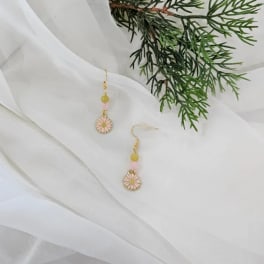 Pair of floral drop earrings on white fabric with greenery nearby