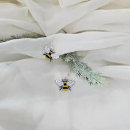 White fabric with two bee-shaped dangling earrings and faux greenery