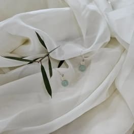 White fabric with two dangling blue bead earrings and a few green leaves