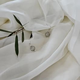 White fabric with small silver earrings and a sprig of green leaves