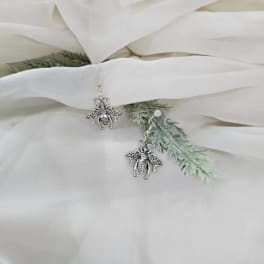 Bee-shaped earrings on white fabric with faux greenery