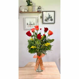 Bouquet of red and orange roses in a glass vase with an orange polka-dot ribbon