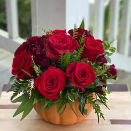 Red roses arranged in a low orange pumpkin-shaped container