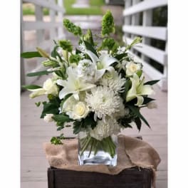 White floral arrangement in a clear glass vase with green accents