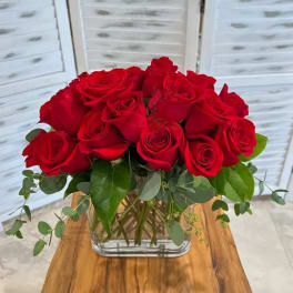 Red roses arranged in a clear glass vase with greenery