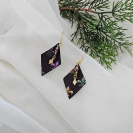 Pair of dangling geometric earrings on white fabric with evergreen sprigs