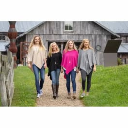 Four women walking outdoors in poncho-style tops in front of a barn