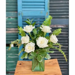 White roses arranged in a green glass vase with fern-like greenery