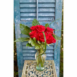 Red roses in a clear glass vase with greenery