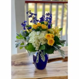 Yellow roses and white hydrangeas in a blue vase with purple flowers