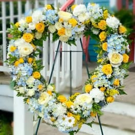 Heart-shaped floral wreath with yellow, white, and blue flowers on a stand