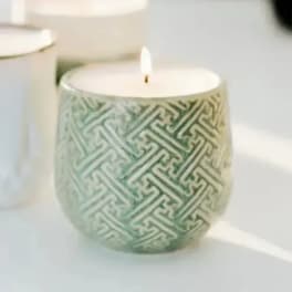 Patterned candle in a ceramic holder with a lit wick