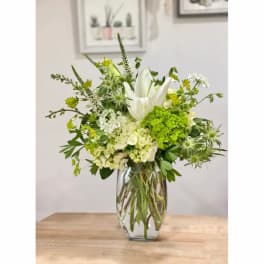 White lilies and green flowers arranged in a clear glass vase