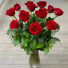 Red roses arranged in a clear glass vase with mixed greenery