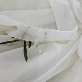 White fabric with pearl drop earrings and a few green leaves