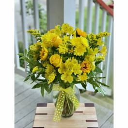 Yellow mixed bouquet in a glass vase with a polka-dot ribbon
