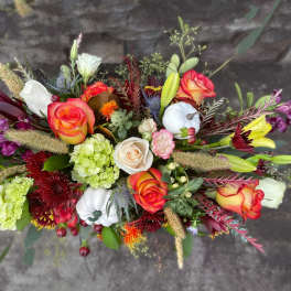 Elongated fall flower arrangement with orange roses, yellow lilies, green hydrangeas, and white pumpkins.