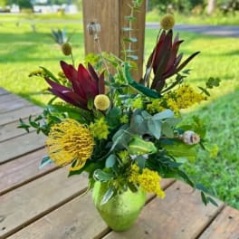 Mixed floral arrangement in a green vase with yellow and burgundy blooms