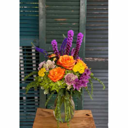 Orange roses and purple flowers in a clear glass vase