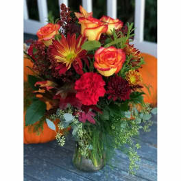 Autumn bouquet of orange roses, red mums, and carnations in a glass vase