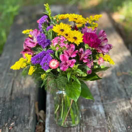 Mixed bouquet of yellow daisies, purple statice, and pink alstroemeria in a glass vase