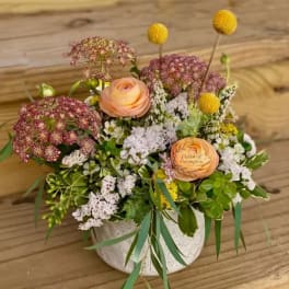 Mixed floral arrangement in a white vase with peach blooms and yellow accents
