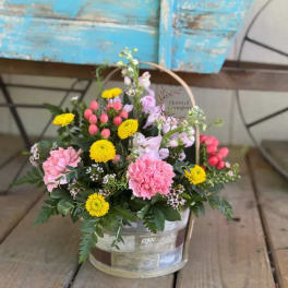 Pink and yellow mixed flower arrangement in a handled basket