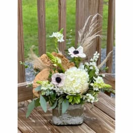 White floral arrangement in a rustic container with dried grasses and wood slices