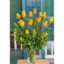 Yellow roses arranged in a clear glass vase with greenery