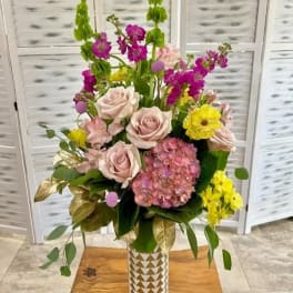 Mixed bouquet of pale pink roses, yellow blooms, and magenta flowers in a patterned vase