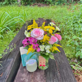 Pink roses and yellow flowers arranged in a glass vase with a candle and gift box
