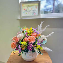 Mixed bouquet of peach roses and purple flowers in a white container