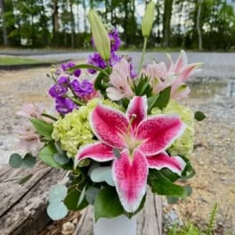 Pink lilies and purple flowers in a clear vase with green hydrangeas