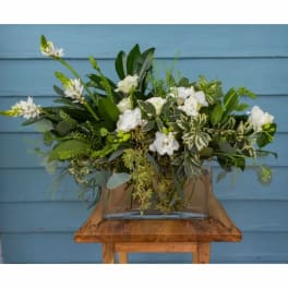 White floral arrangement in a clear rectangular vase on a wooden table