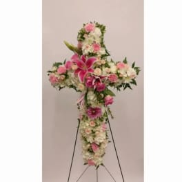 Cross-shaped floral tribute with pink and white flowers on a stand