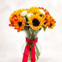 Sunflower bouquet in a clear glass vase with a red ribbon