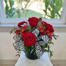 Red roses arranged in a black vase with zebra-print ribbon accents