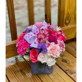 Pink and purple mixed flower arrangement in a square vase with heart decorations