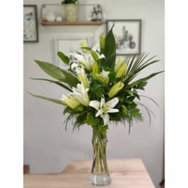 White lilies arranged in a clear glass vase with green foliage