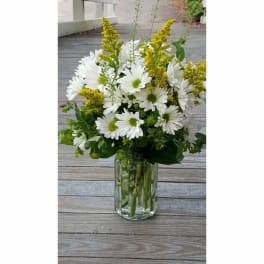 White daisy bouquet with yellow filler in a clear glass vase
