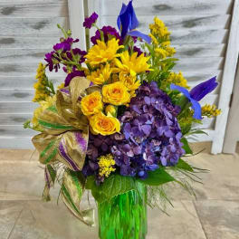 Colorful bouquet with yellow daisies, purple hydrangeas, and roses in a green vase