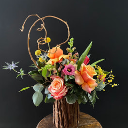 Colorful floral arrangement in a rustic wood vase with curly branches